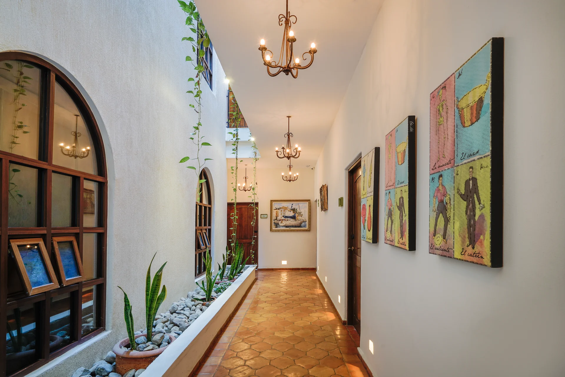 Pasillo de Hotel Galería Guaycura con obras de arte, plantas y puertas arqueadas de madera