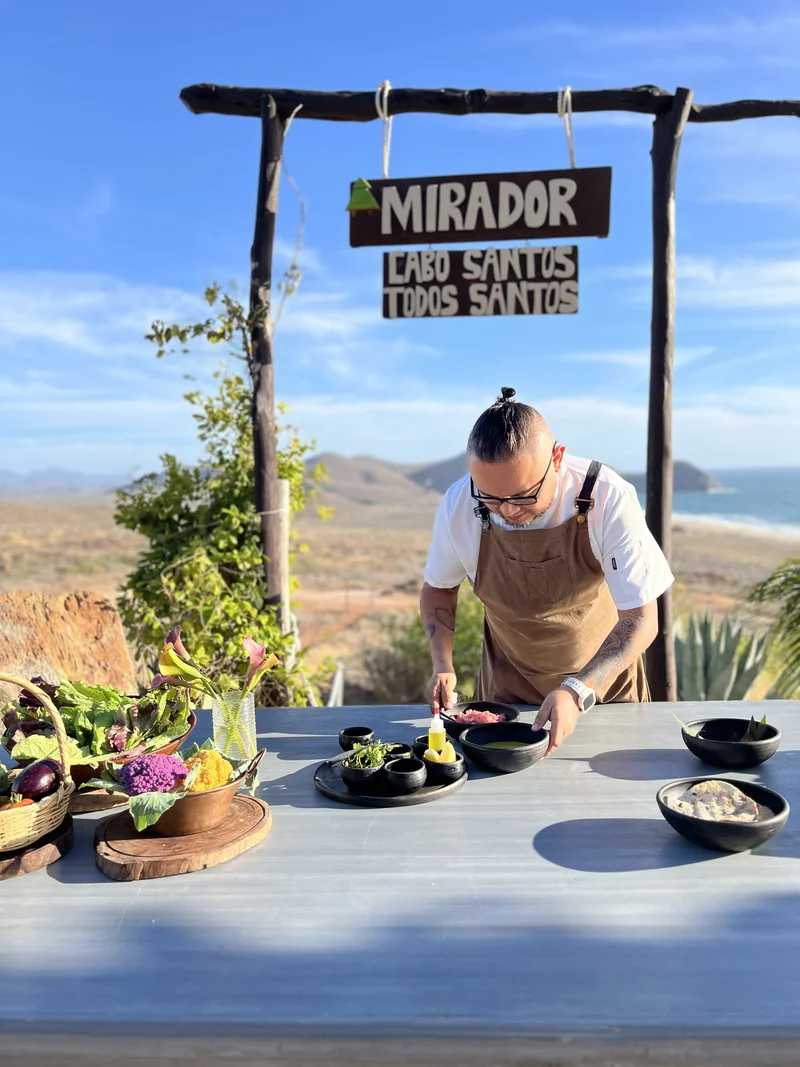 Chef preparando ingredientes locales frente al paisaje de Todos Santos