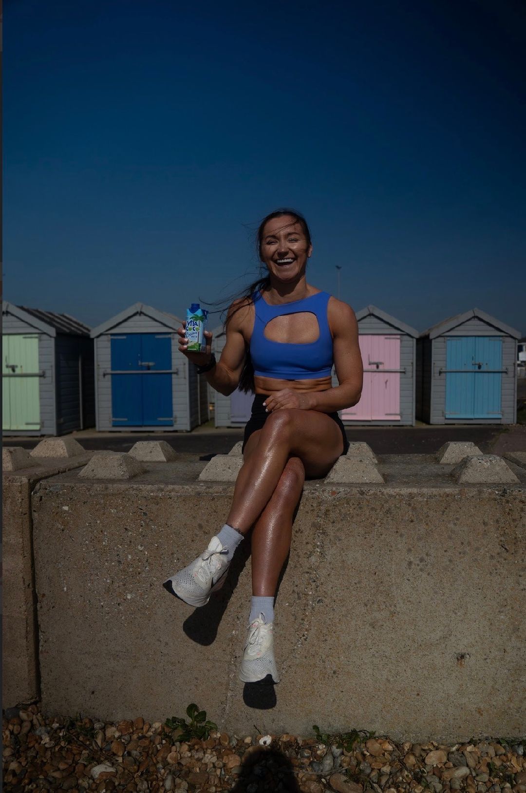 Allana Falconer laughing on the sea wall in front of the beach huts