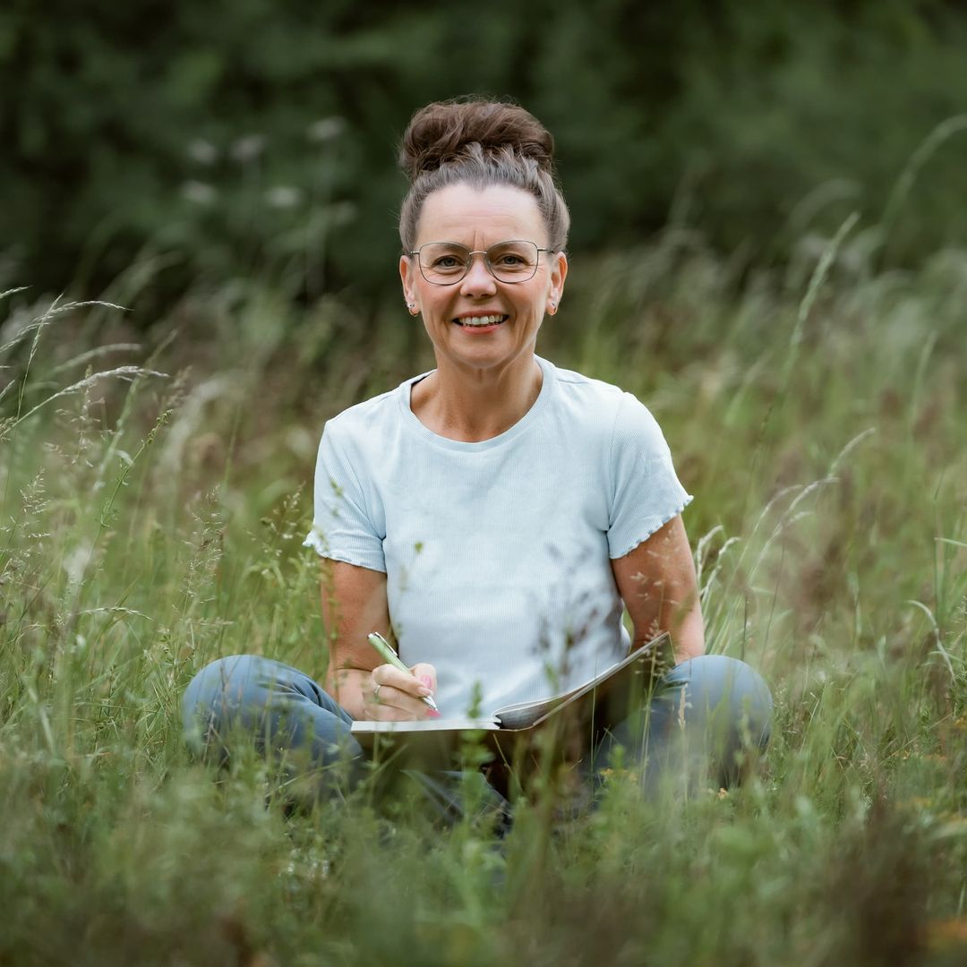 Kati Kreyser sitzt mit Stift und Redemappe in einer Wiese