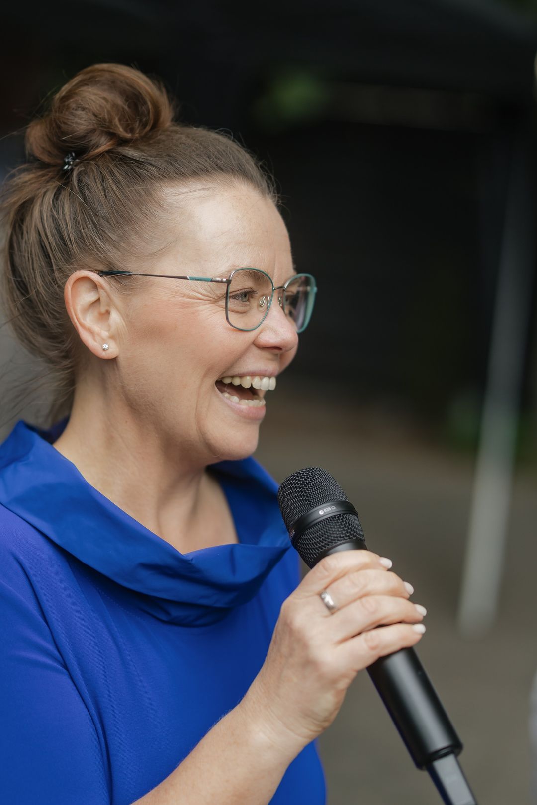 Kati Kreyser lacht mit dem Mikrofon in der Hand während einer freien Trauung