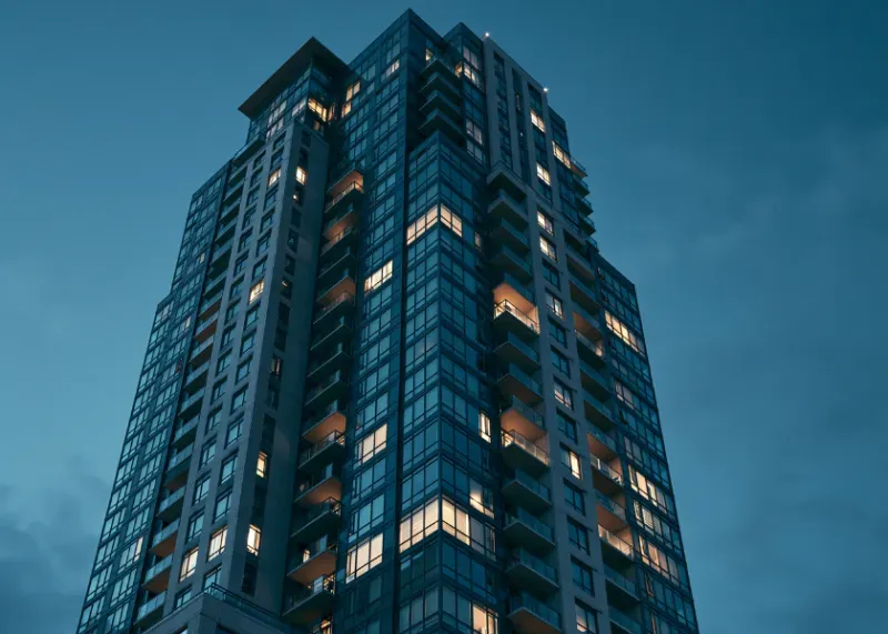 High-rise residential apartment tower with lit balconies at dusk