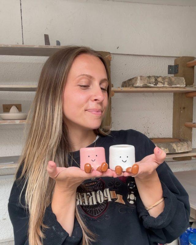 kit in the pottery studio holding two little smiley marshmallow pots