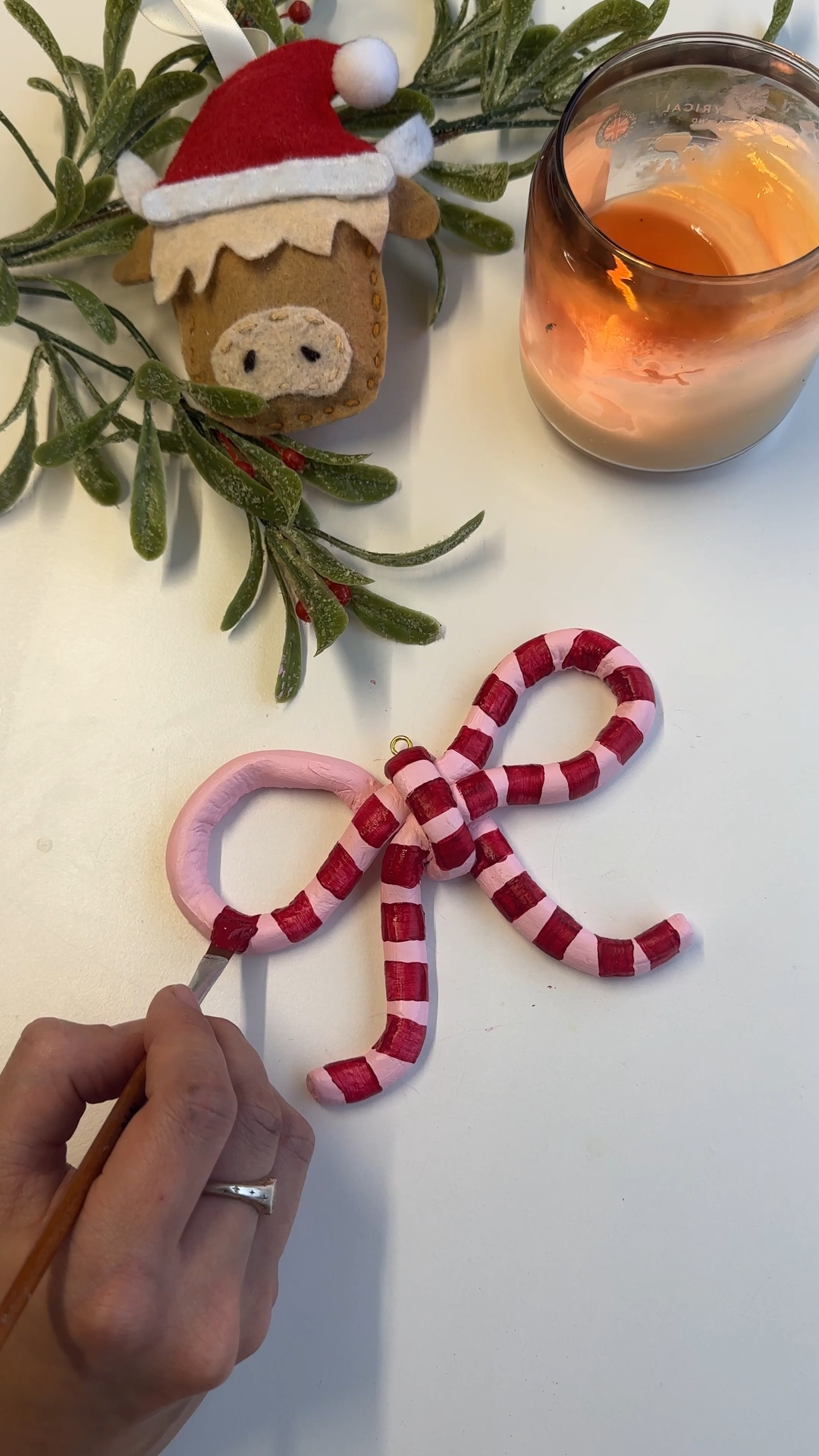 a large handmade clay bow decoration painted in red and pink stripes, hanging from a cream ribbon