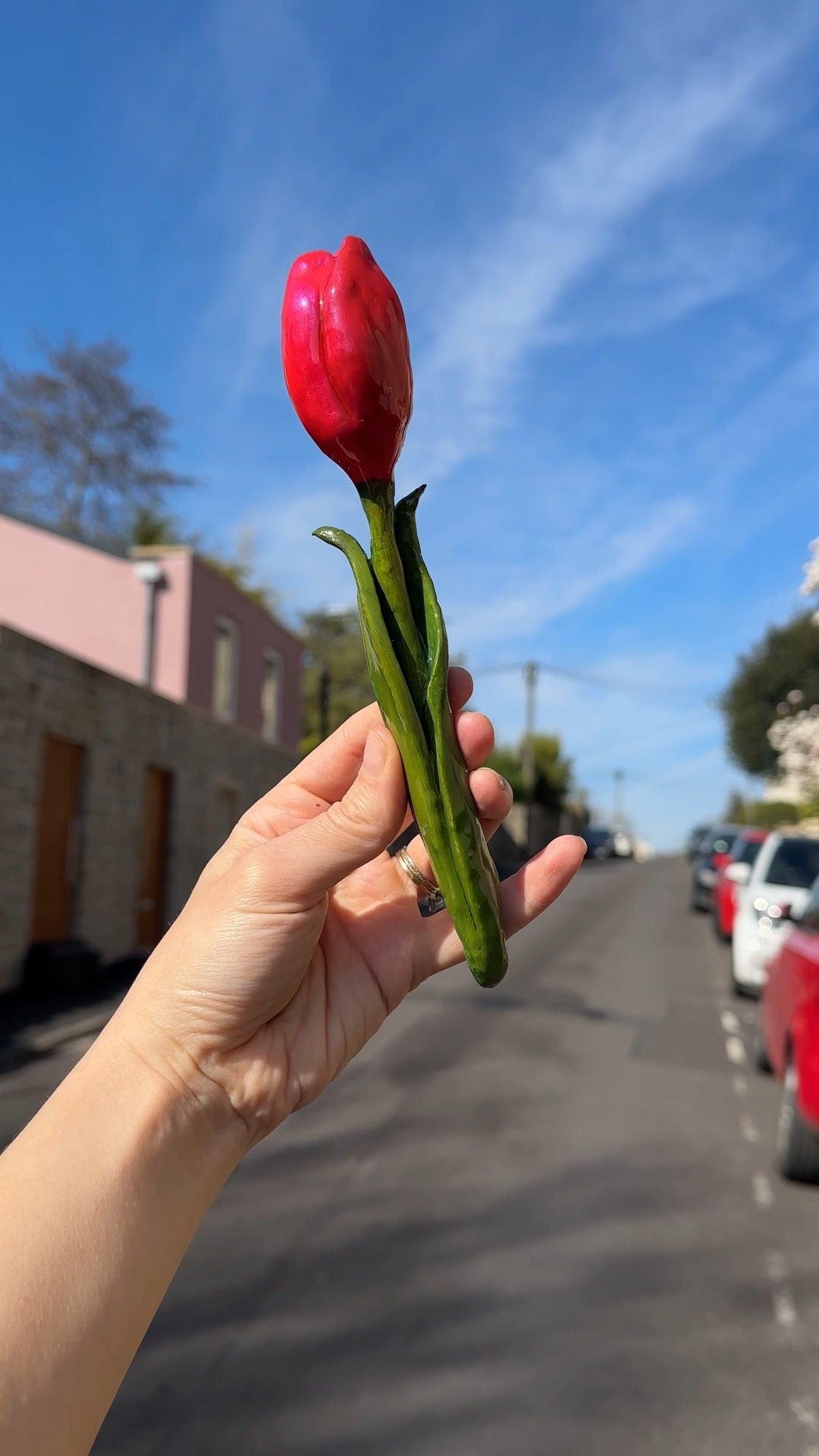 a handmade red clay tulip on a green stem, held up against a blue sky