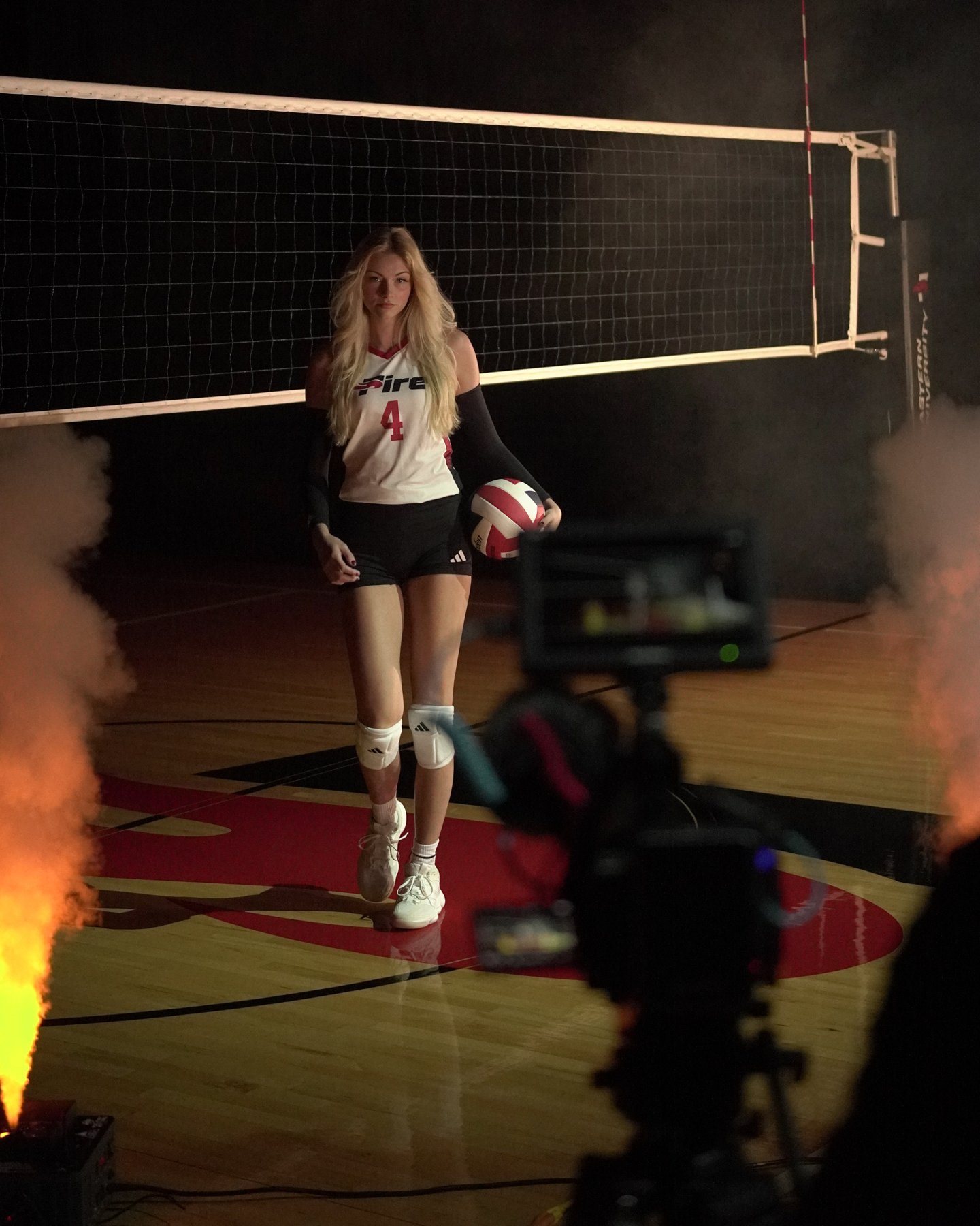 Behind the scenes of the SEU Fire Volleyball shoot, with a player at the net, a camera, and dramatic lighting