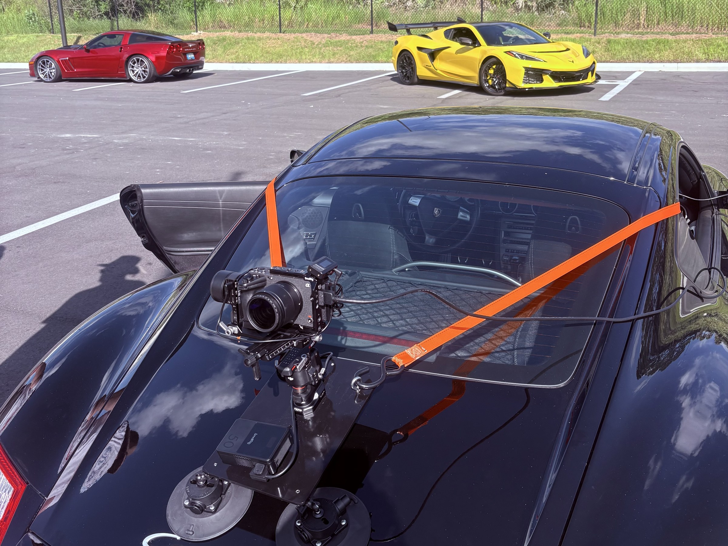 Camera rig mounted on a black Corvette during a production, with red and yellow Corvettes behind it