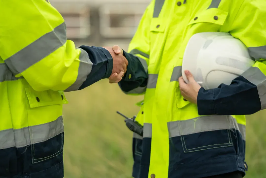 Two workers in high-visibility jackets shaking hands