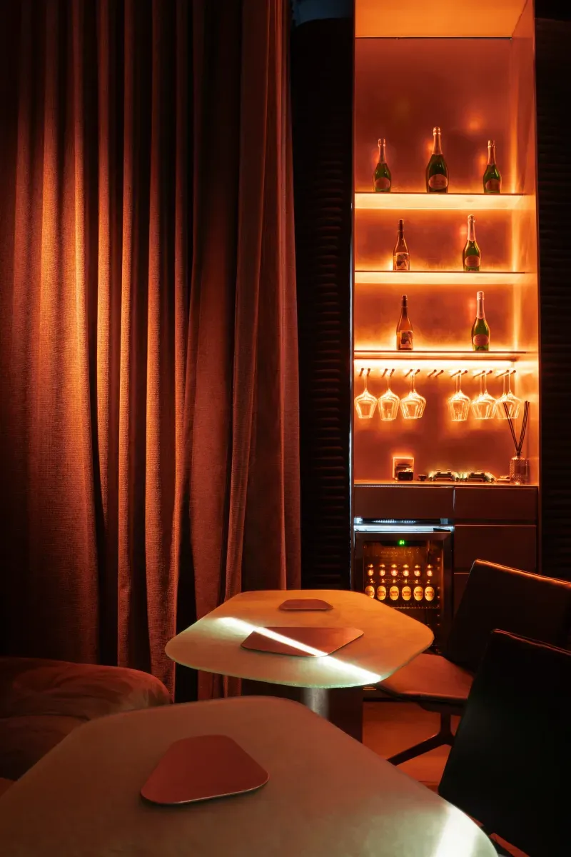 Private room with curved tables, red curtains and illuminated bottle shelves