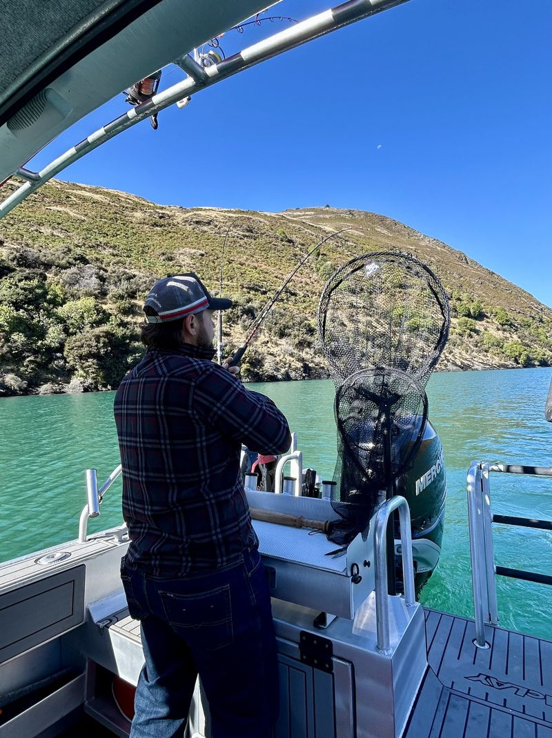 Guide steadies a landing net as a rod bends with a bite on Lake Wānaka