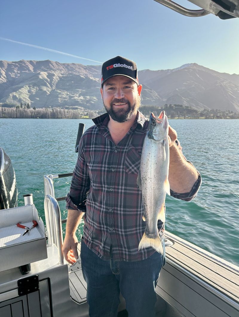 Guest holding up a salmon catch with the Southern Alps behind