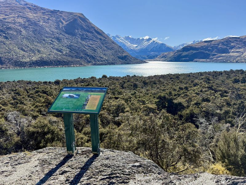 DOC signboard overlooking the turquoise waters of Lake Hāwea and the mountains beyond
