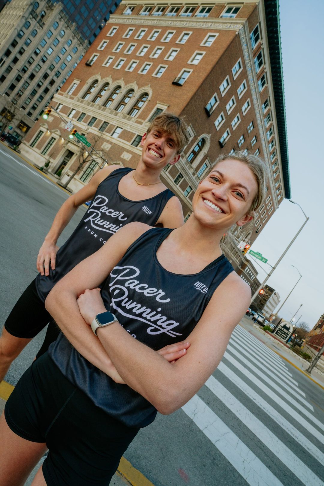 Two Pacer Running athletes smiling at a downtown Indianapolis crosswalk