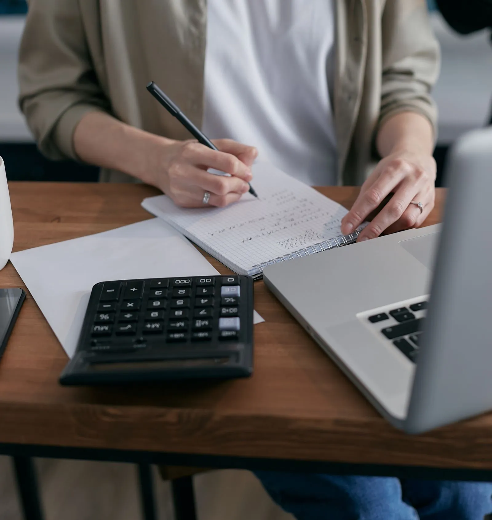 Person reconciling accounts with a calculator and notebook beside a laptop