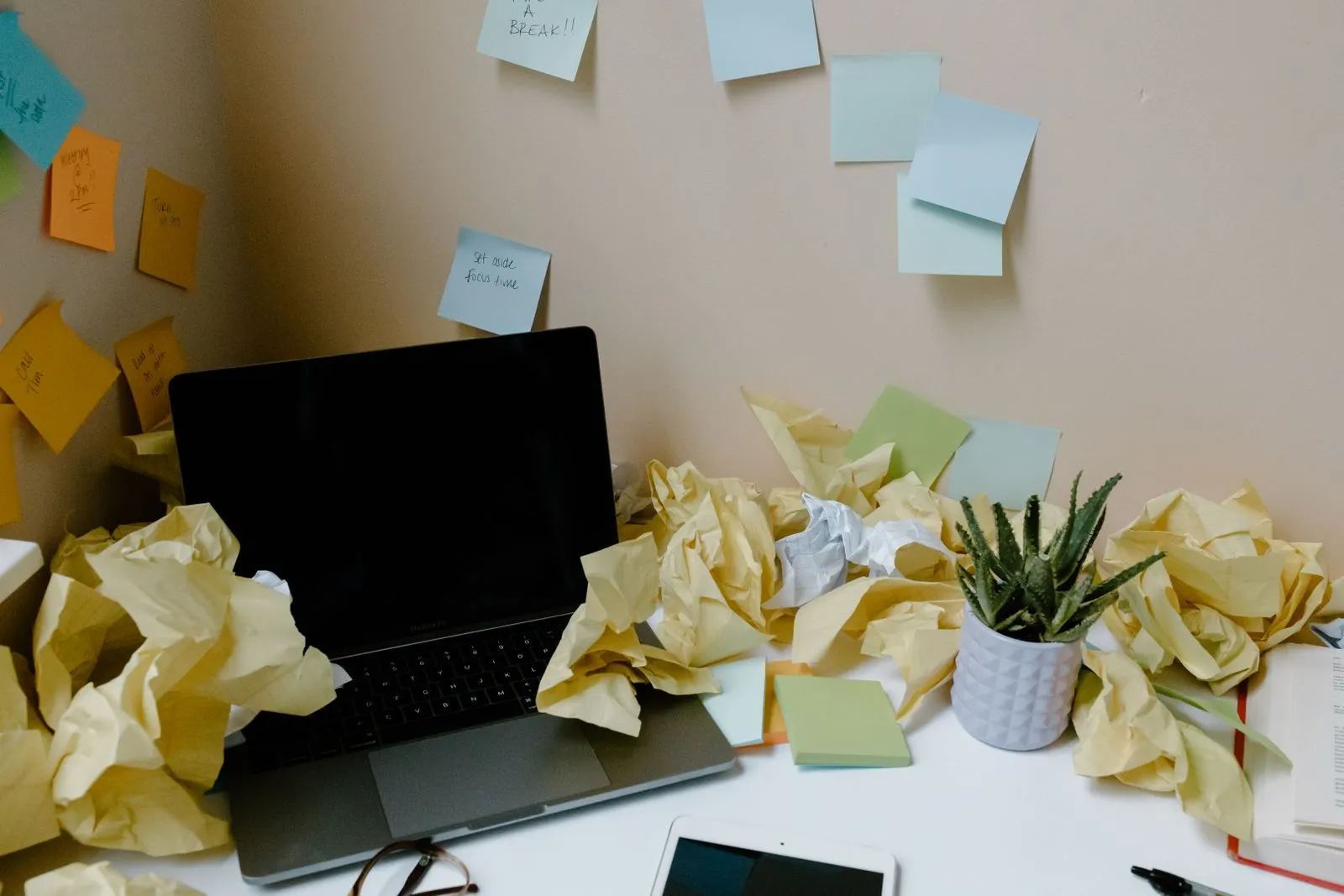 A laptop surrounded by scattered paper notes, representing books that have fallen behind