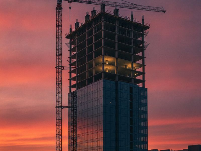 A mid-rise building half complete under a tower crane at dusk