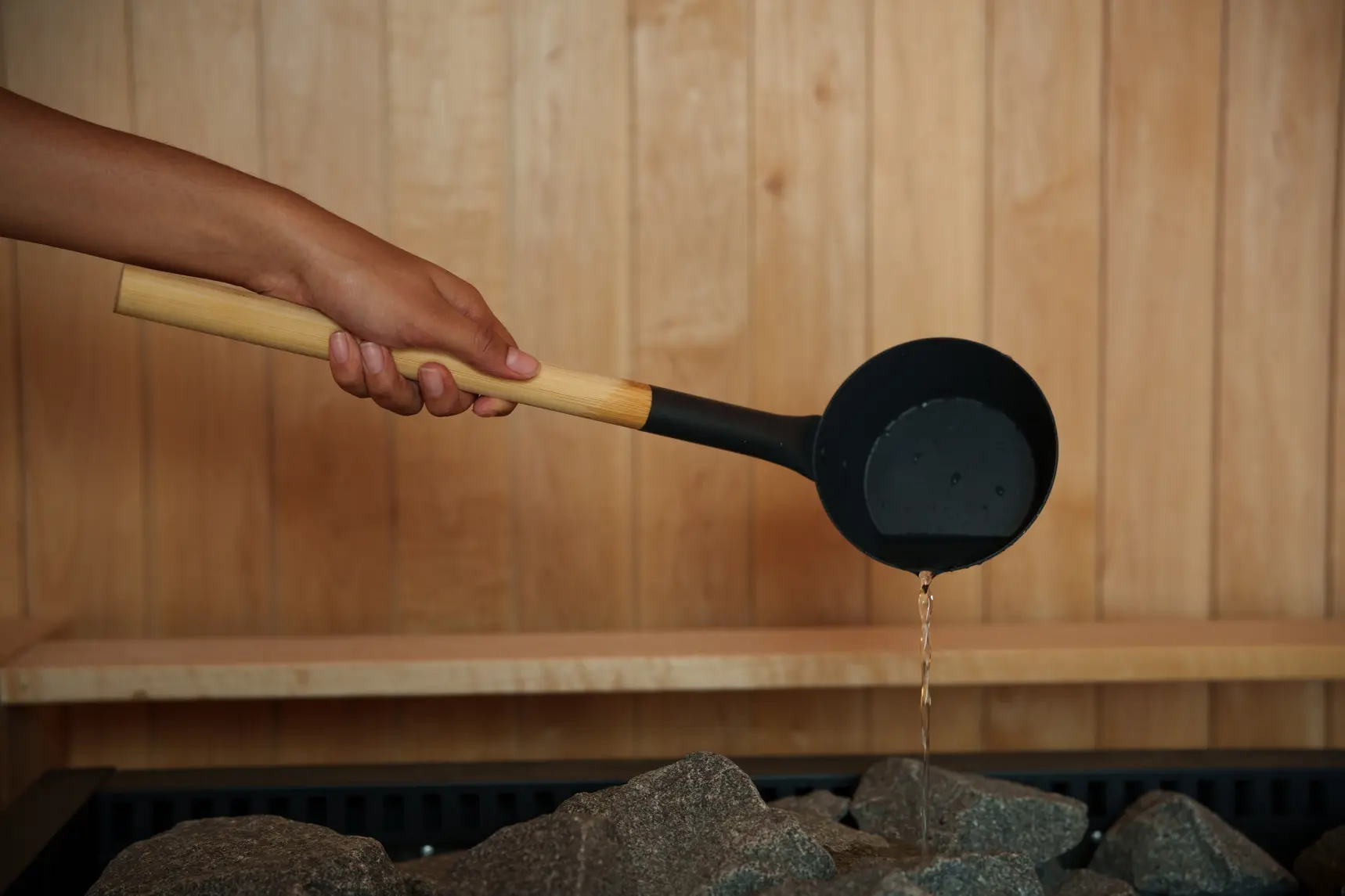Ladle pouring water over sauna stones at Sauna Summit