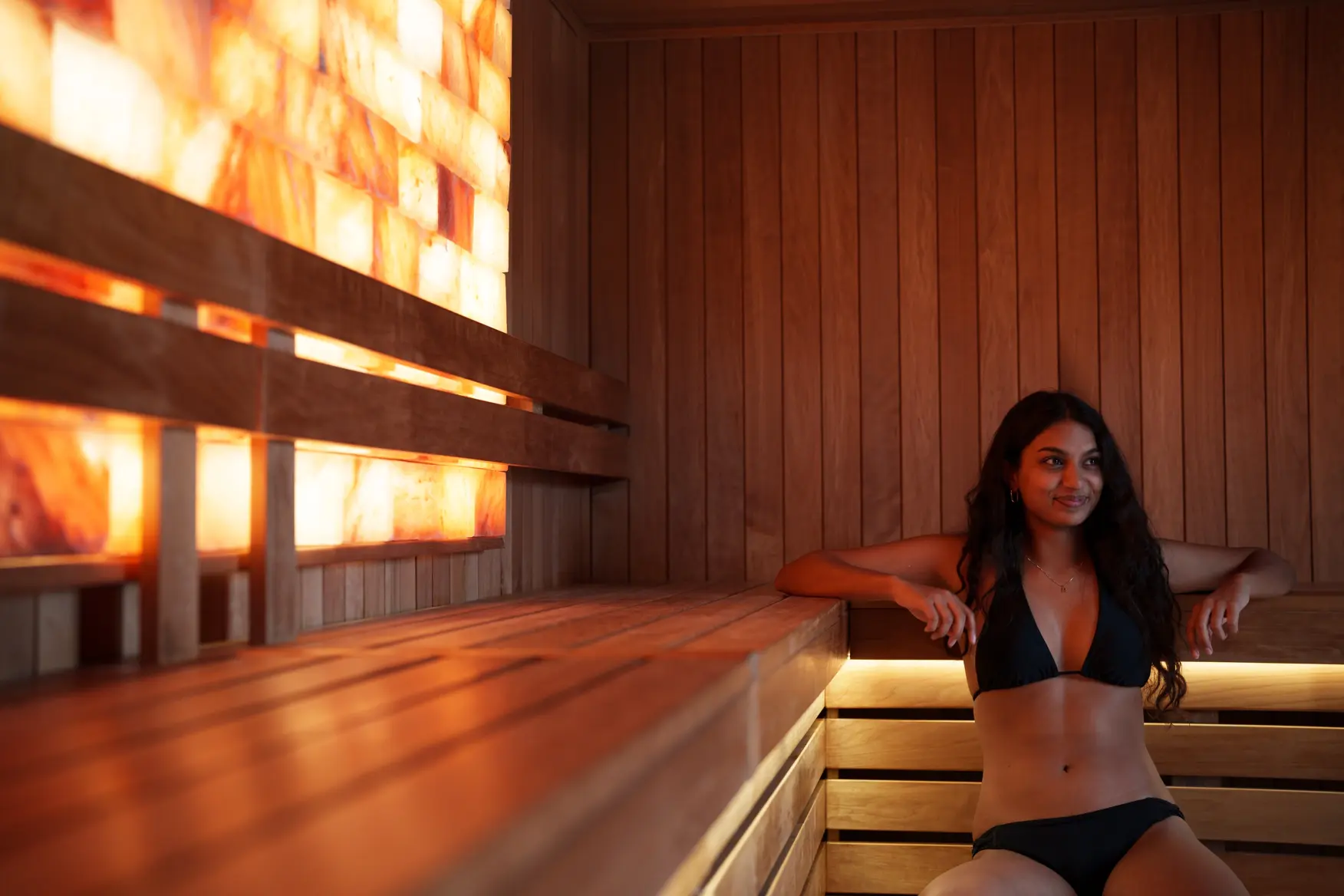 Woman relaxing on a cedar sauna bench beside an illuminated salt wall