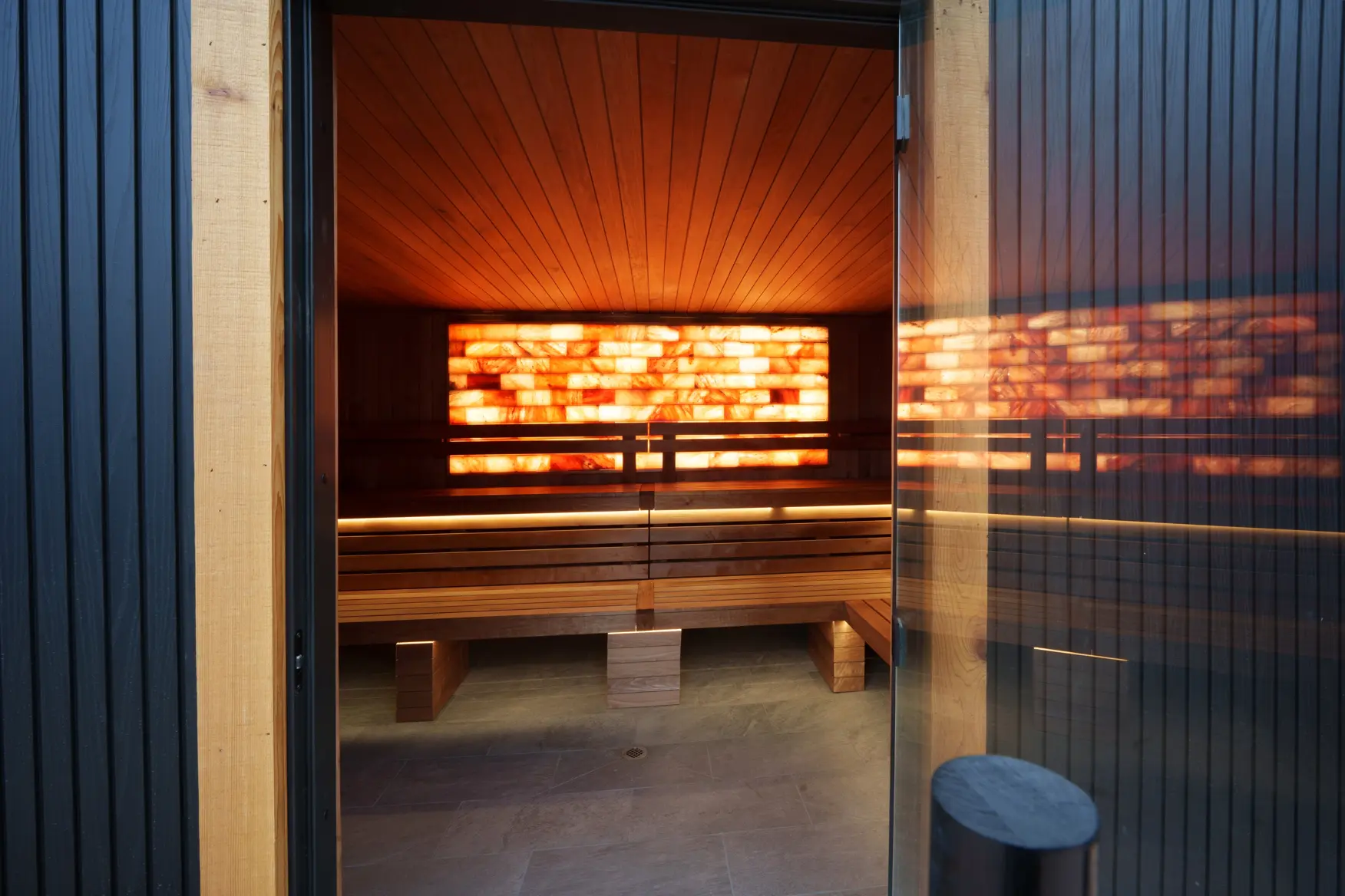 Communal sauna with illuminated salt wall viewed through glass doors