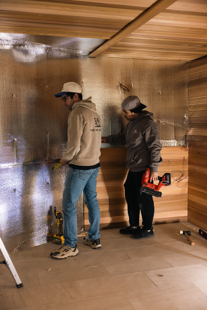Two installers fitting cedar wall panels inside the Bountiful sauna