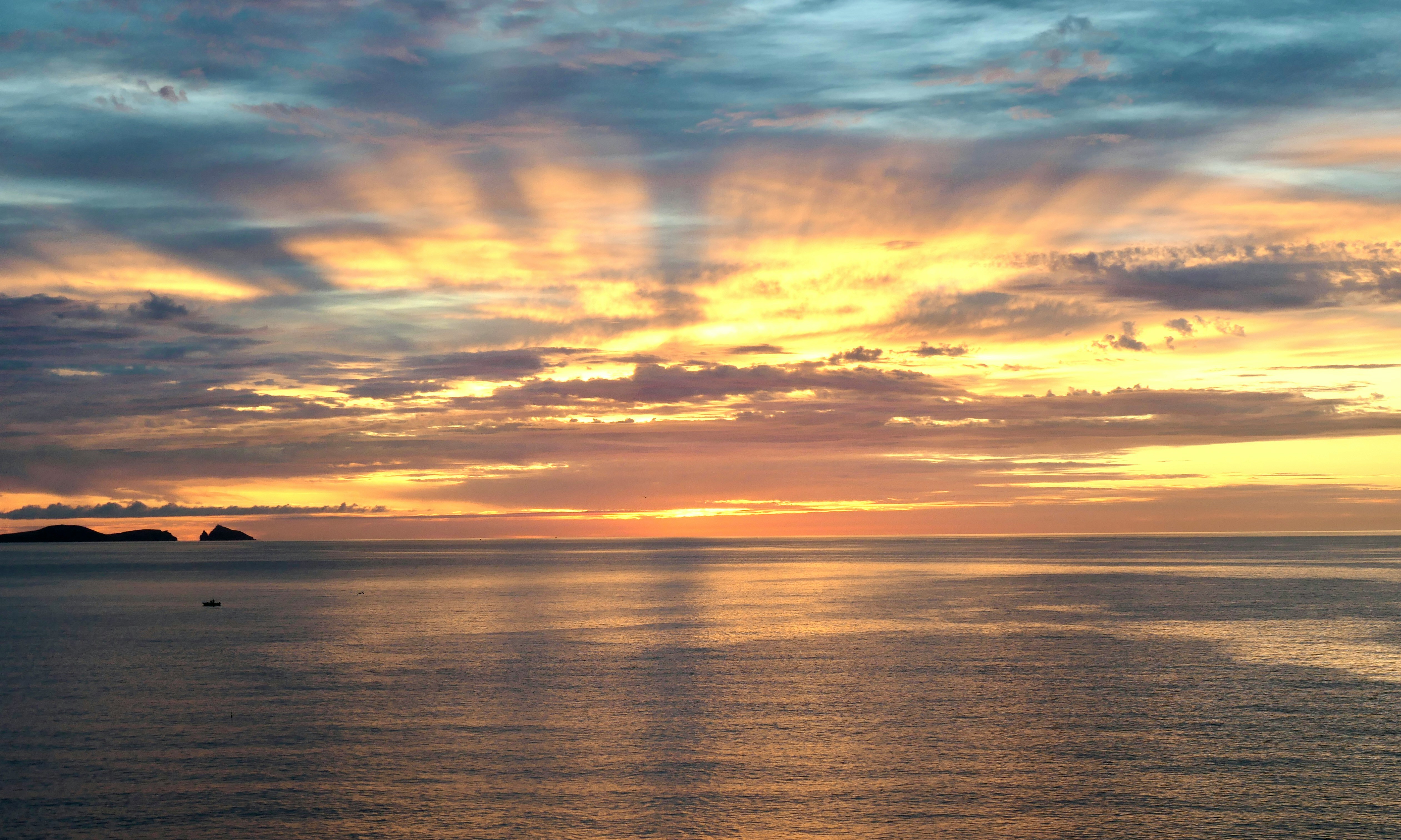 Sunrise over open water, light breaking through cloud cover