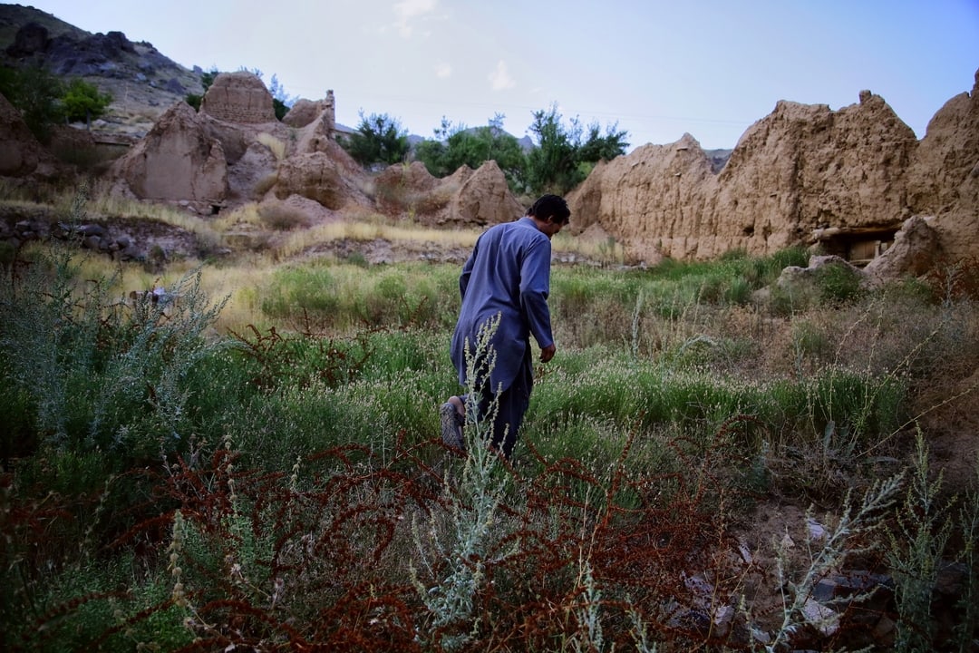 A person walks through the remains of earthen buildings.