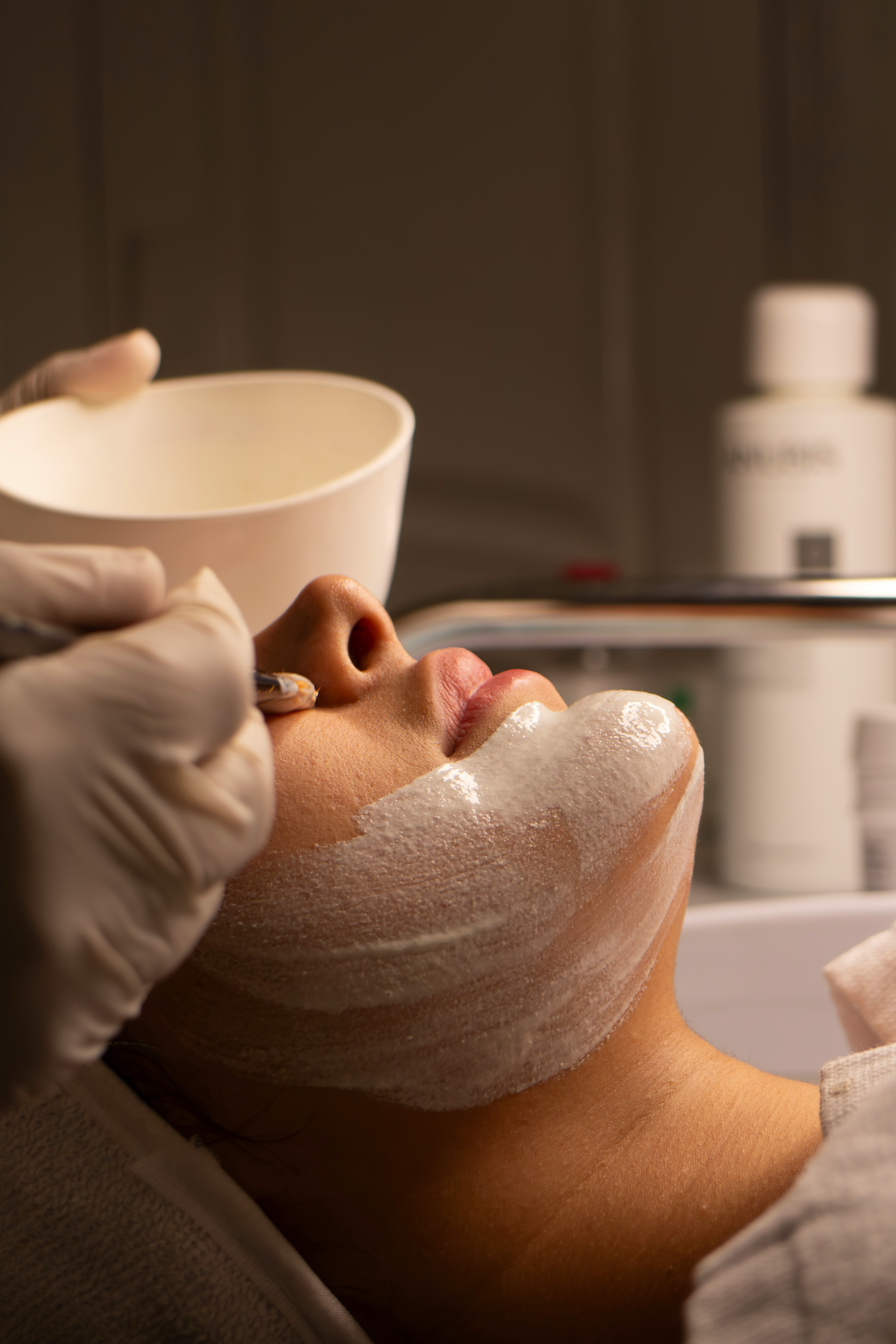 A professional facial mask being applied with a brush during a treatment
