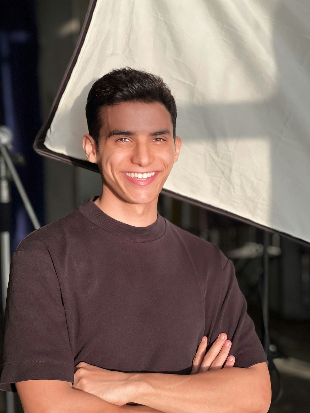 A smiling person with their arms crossed in warm light