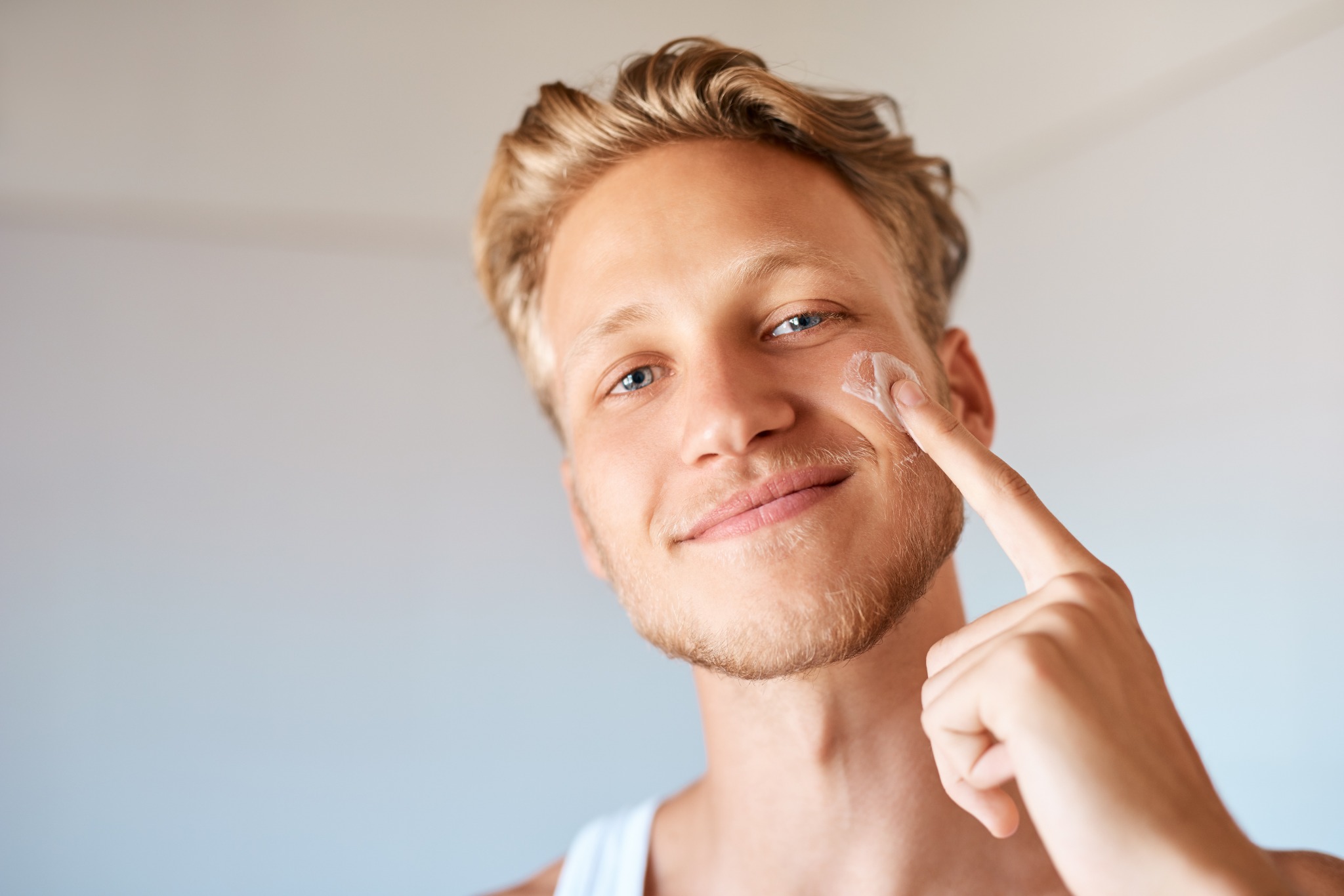 A smiling person applying a small amount of cream to their cheek