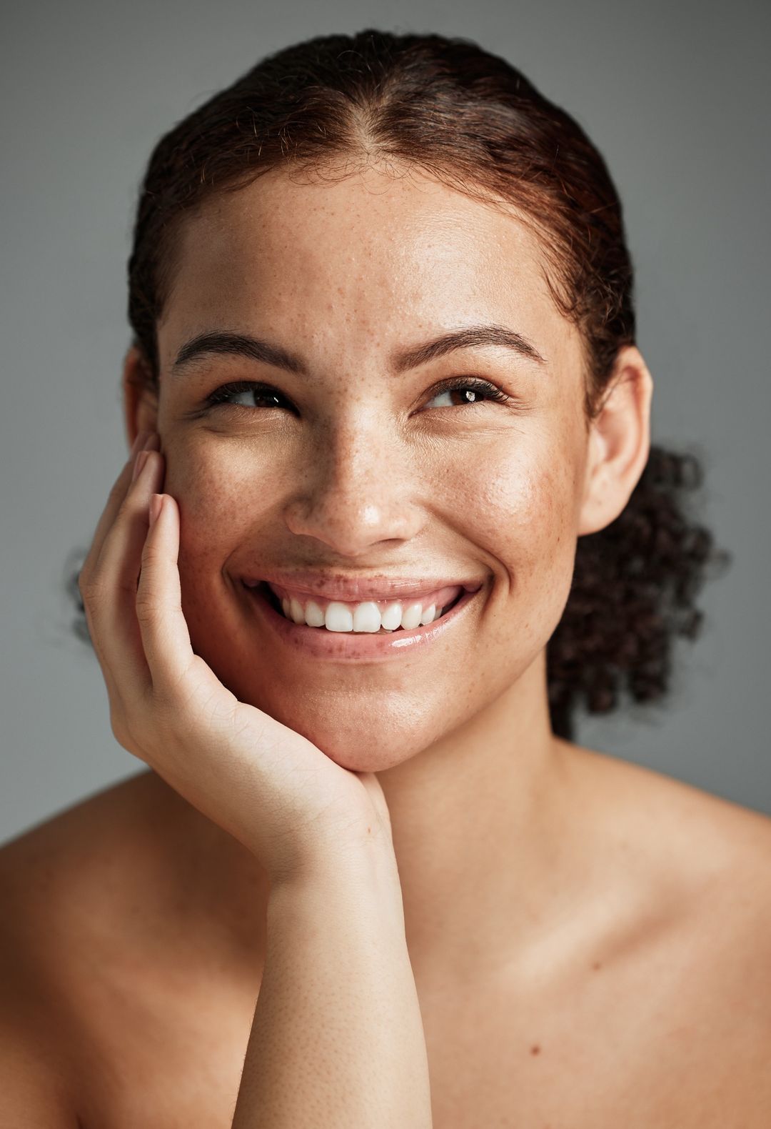 A smiling person resting their cheek on their hand against a grey background