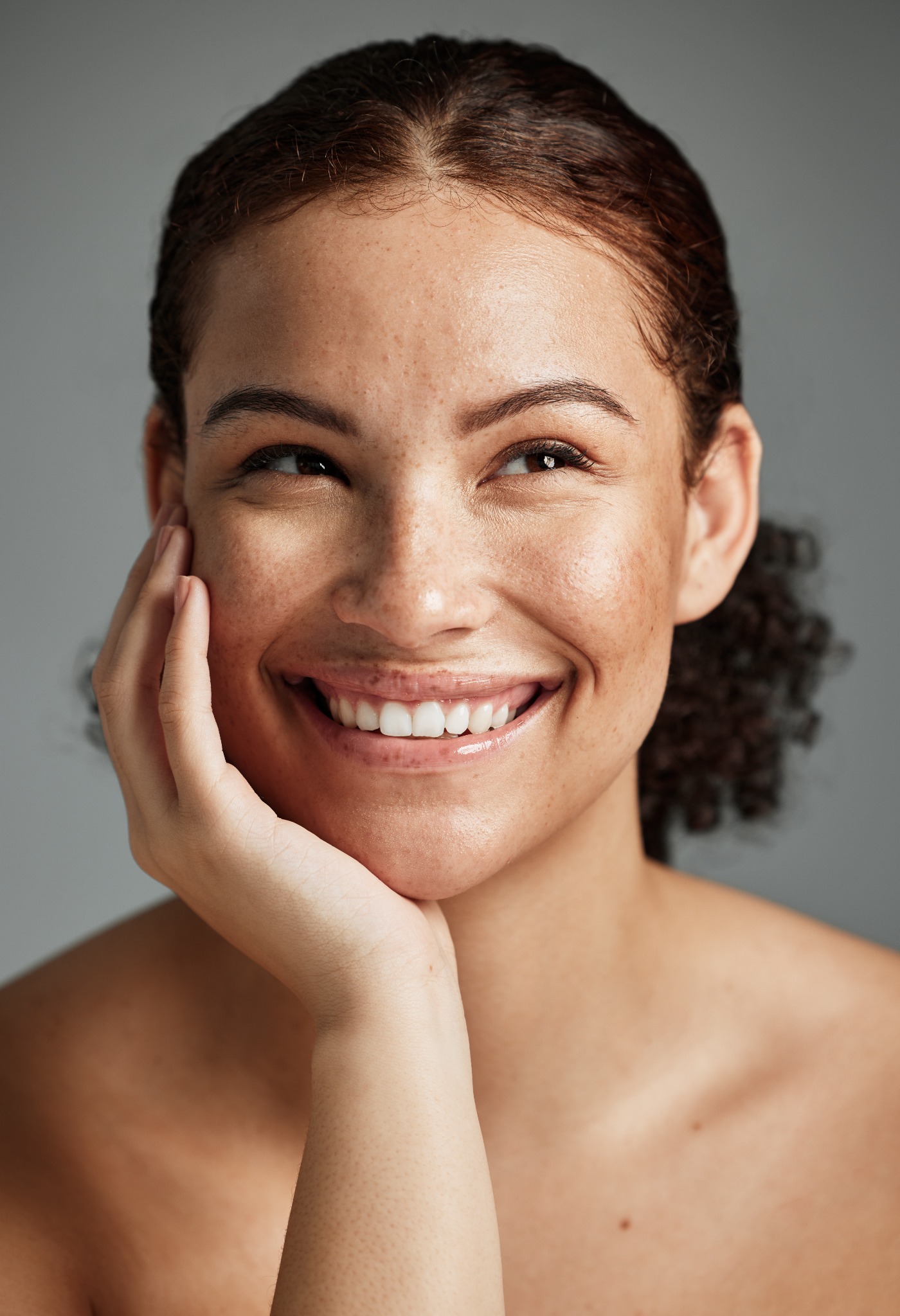 A smiling person resting their cheek on one hand, looking up and away