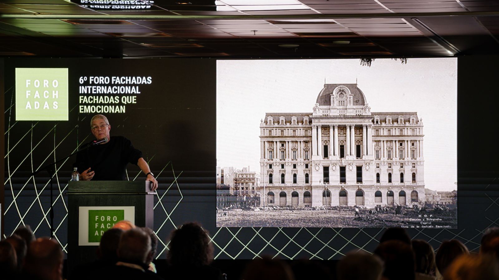 Orador en el atril del foro con una imagen histórica del Palacio de Correos proyectada