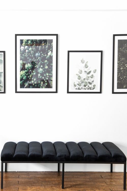 The black bedroom bench beneath three framed botanical illustrations