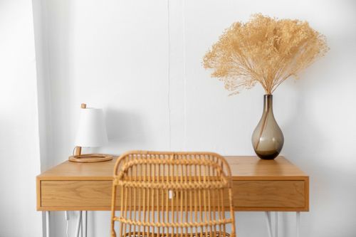 The wooden desk and rattan chair, with a vase of dried flowers