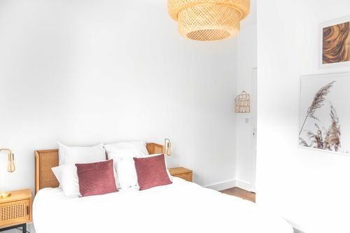 The double bed with red cushions beneath a woven pendant light