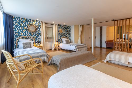 La Chambrée’s shared sleeping area with single beds and a rattan armchair