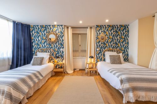 Two single beds in La Chambrée against blue leaf-patterned wallpaper