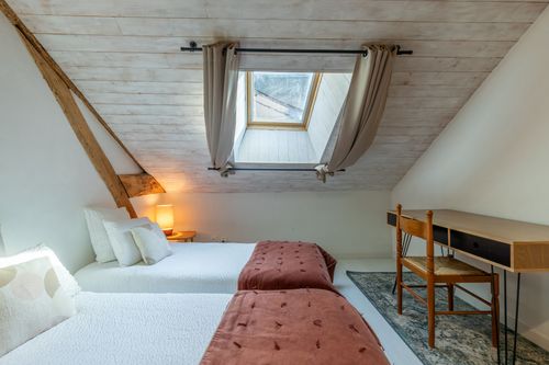 Le Loft’s attic bedroom with single beds and a desk beneath the roof window