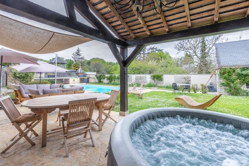 The hot tub beneath the awning, beside the outdoor table, overlooking the garden and pool