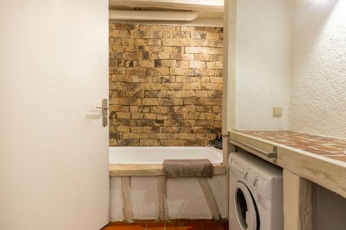 The bathtub against the stone wall and washing machine beneath the worktop