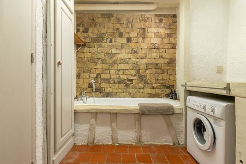 The bathroom with a bathtub, stone wall and laundry area