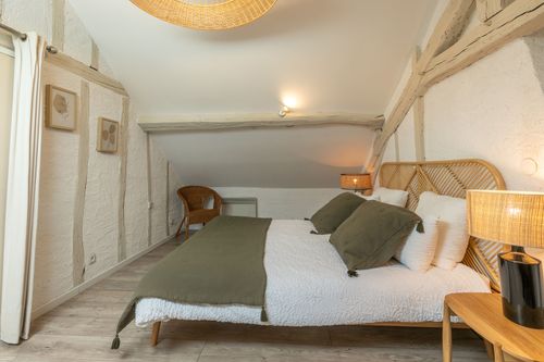 The double bed with a green bedspread beneath white-painted roof beams