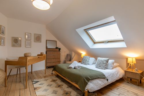 The double bed with a green bedspread beneath the roof window
