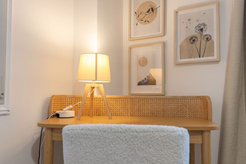 The wood-and-cane desk lit by a lamp beside wall illustrations