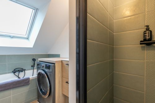 The attic bathroom with a bathtub, washing machine and shower