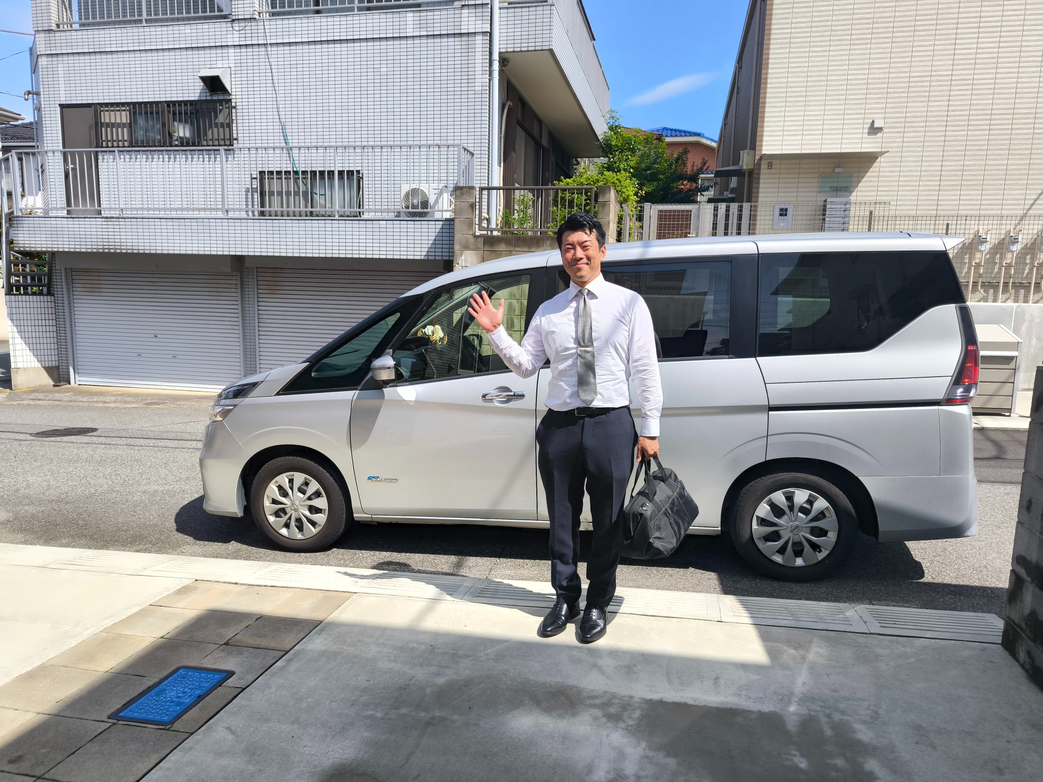 送迎車の前で手を振る平山