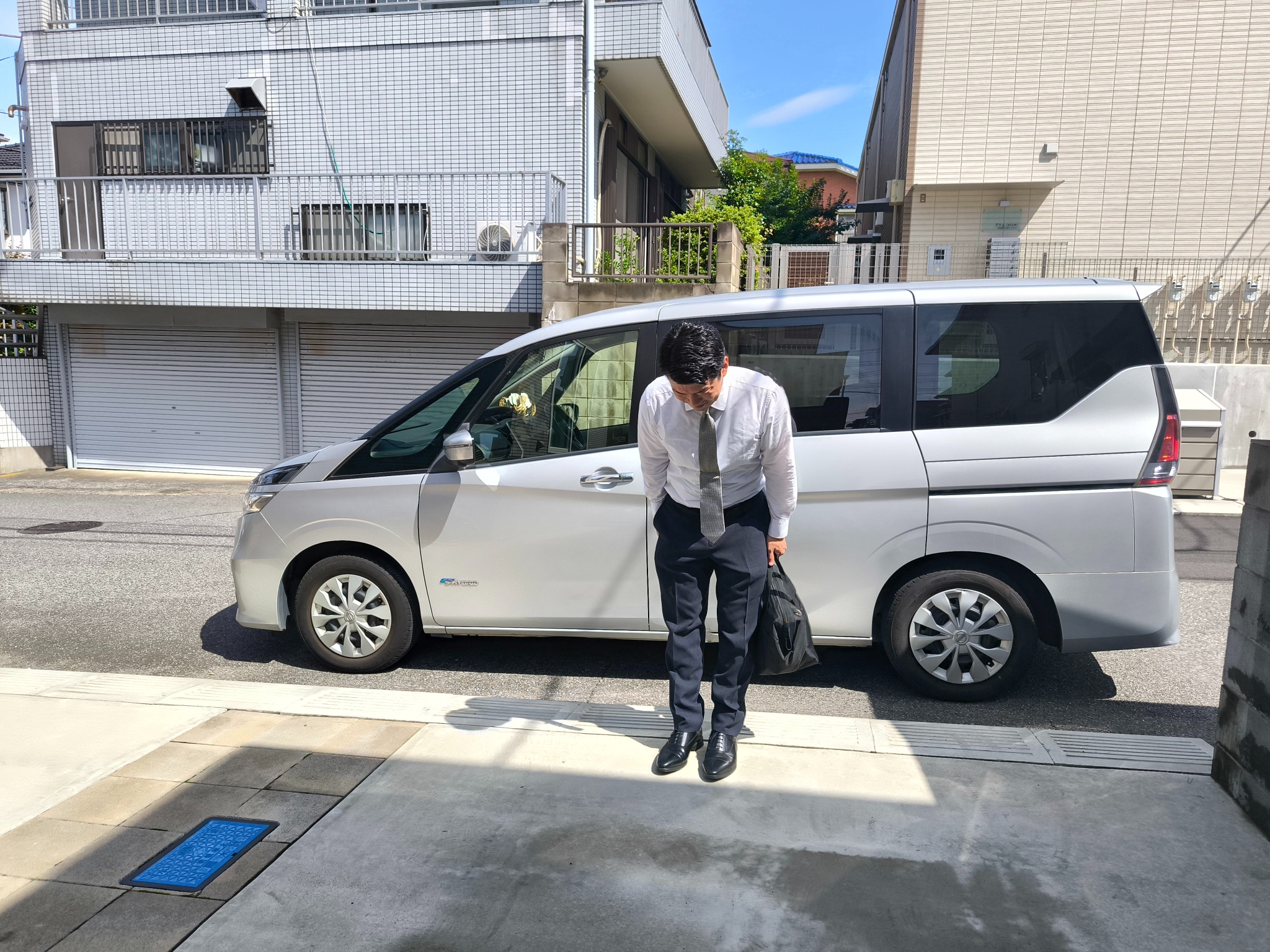 ツアー当日、送迎車の前でお辞儀をして迎える平山