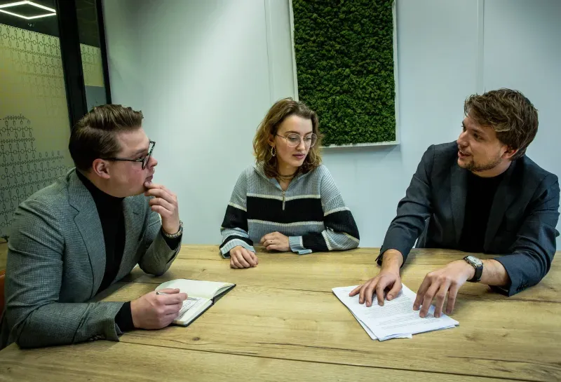 Drie mensen bespreken de ICT-omgeving aan tafel.