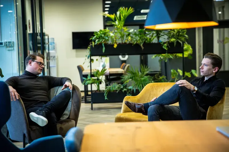 Twee mensen in gesprek in een zithoek op kantoor.