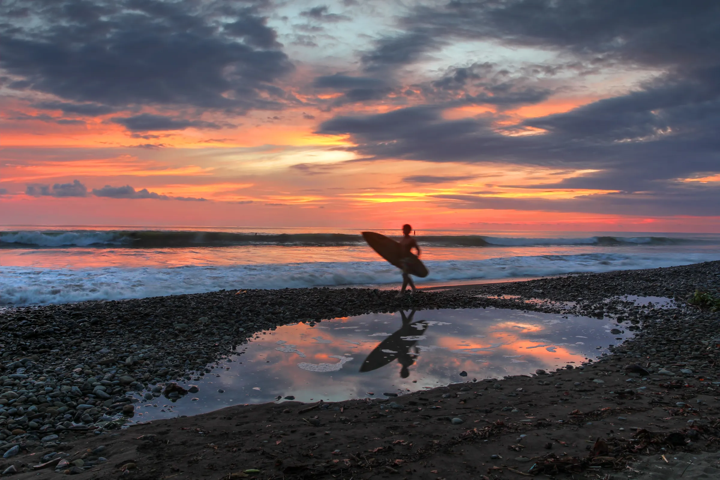 Surfer walking beside a tide pool at sunset, Costa Rica